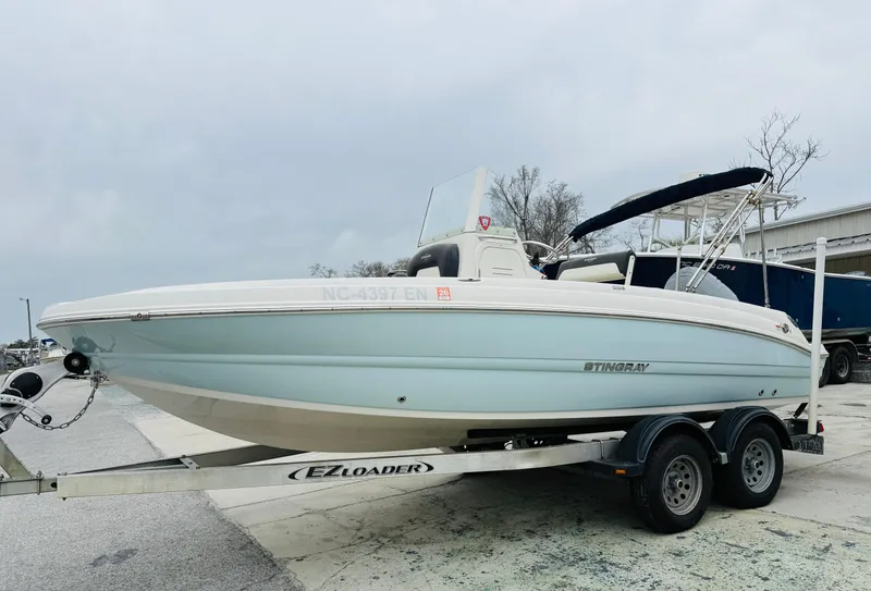 Slide: The Image of 2019 Stingray 206 CC boat on trailer, light blue hull, parked outdoors. - 0