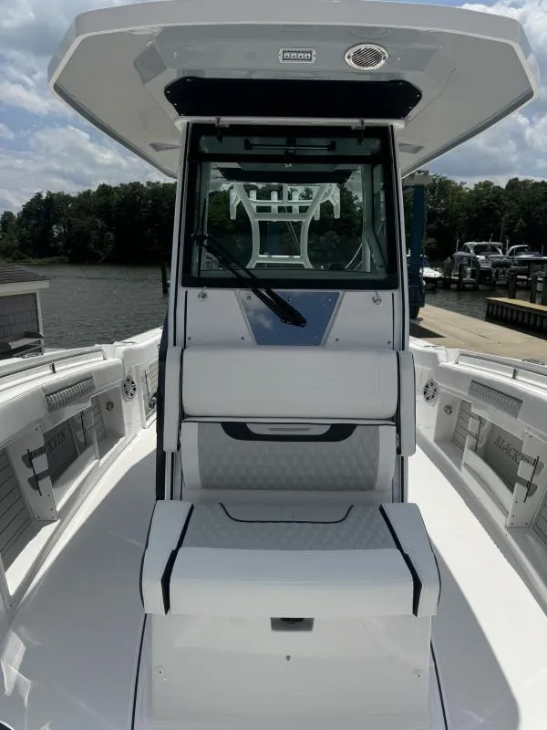 Slide: The Image of 2025 Blackfin 302 CC boat with sleek white seating and console, docked by a serene waterfront. - 14