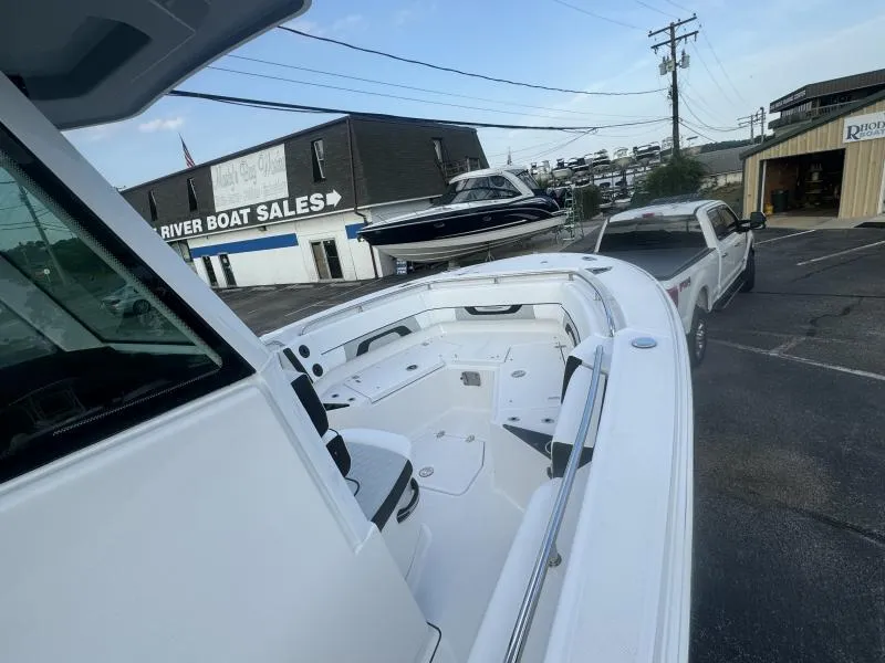 Slide: The Image of 2025 Blackfin 252 CC boat at dealership, parked near truck and boat sales building. - 8