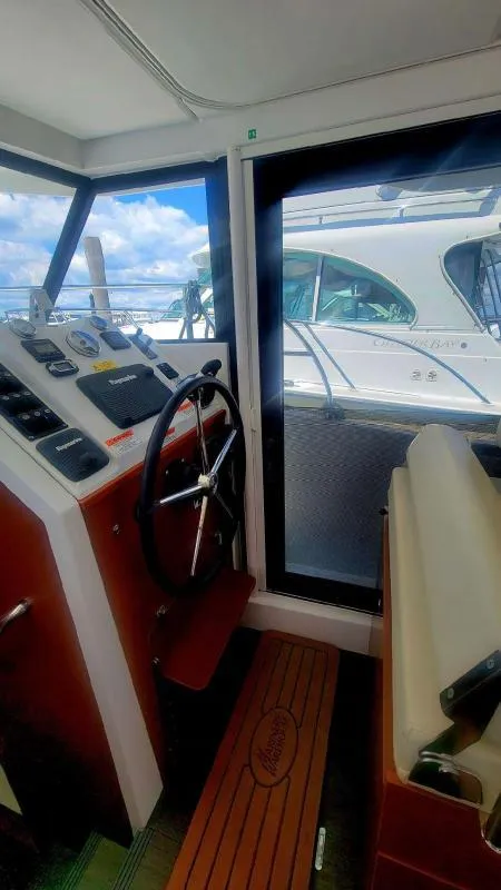 Slide: The Image of 2017 Beneteau Swift Trawler 30 helm with steering wheel and control panel, docked beside another boat. - 10