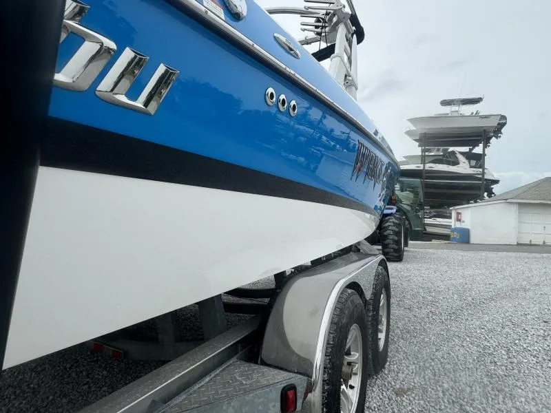 Slide: The Image of 2013 Malibu Wakesetter 23 LSV boat on trailer, blue and white design, parked near other boats. - 12