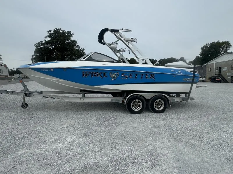 Slide: The Image of 2013 Malibu Wakesetter 23 LSV boat on trailer, blue and white design, parked outdoors. - 2