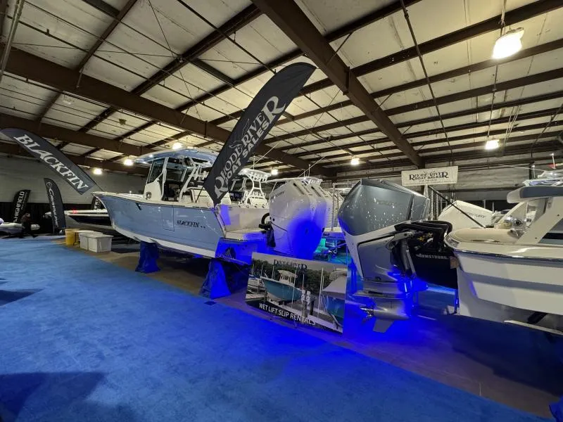 Slide: The Image of 2025 Blackfin 332 boat displayed indoors with promotional banners and blue lighting. - 3