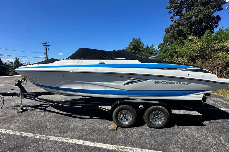 Slide: The Image of 2023 Crownline 240 SS boat on trailer, parked outdoors under clear blue sky. - 2