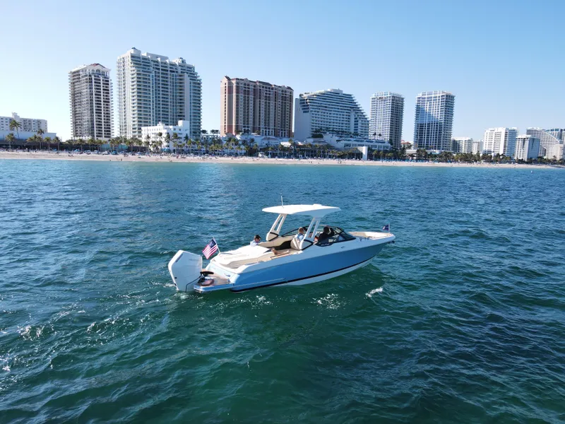 Slide: The Image of 2025 Chris-Craft Sportster 28 boat cruising near a city skyline and beach. - 3