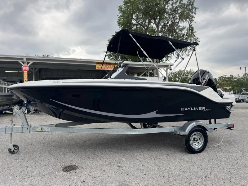 The Image of 2025 Bayliner Element M17 boat on trailer, black hull, bimini top, parked outdoors. - 0