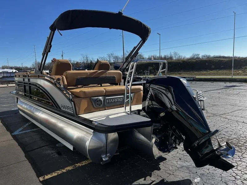 Slide: The Image of 2024 Harris Solstice 230 pontoon boat with canopy and outboard motor in a parking lot. - 7