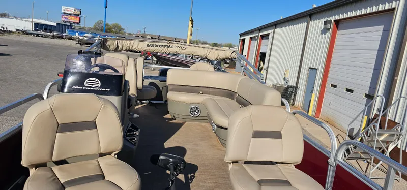 Slide: The Image of 2024 Sun Tracker BB-18 pontoon boat with beige seating, docked near a warehouse. - 5