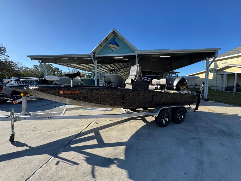 Slide: The Image of 2023 Xpress H22B boat on trailer under sunny sky, parked near a covered structure. - 2