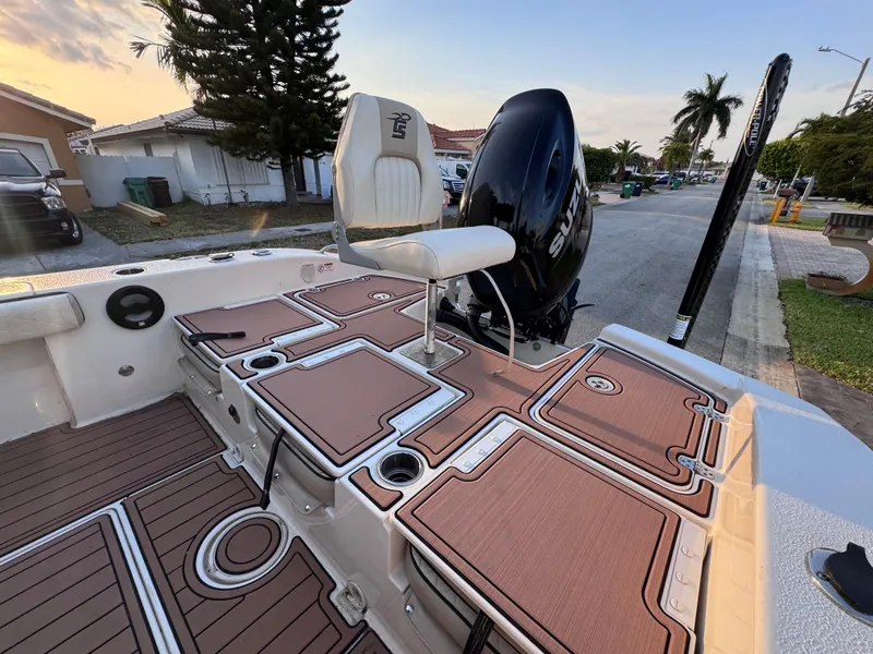 Slide: The Image of 2021 Carolina Skiff Ultra Elite 24 boat deck with seating and motor, parked near palm trees. - 27