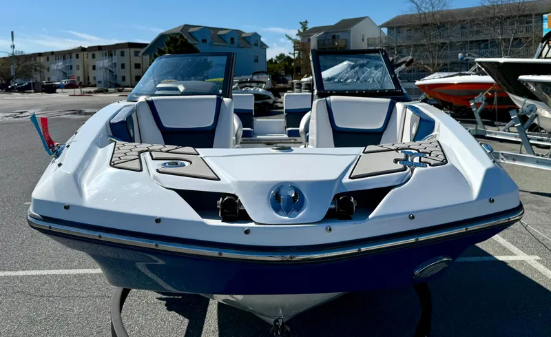 Slide: The Image of 2020 Scarab 215 ID boat, white and blue, parked in a marina with buildings in the background. - 7