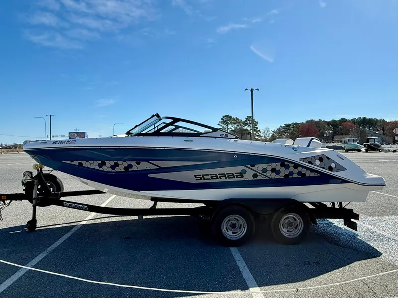 Slide: The Image of 2020 Scarab 215 ID boat on trailer in parking lot under clear blue sky. - 9