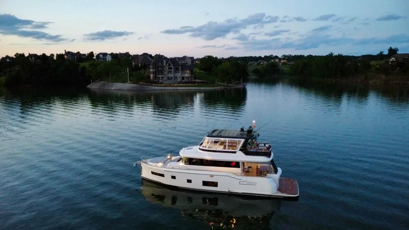 Slide: The Image of 2021 Sirena 58 yacht cruising on a serene lake at dusk, with houses in the background. - 3