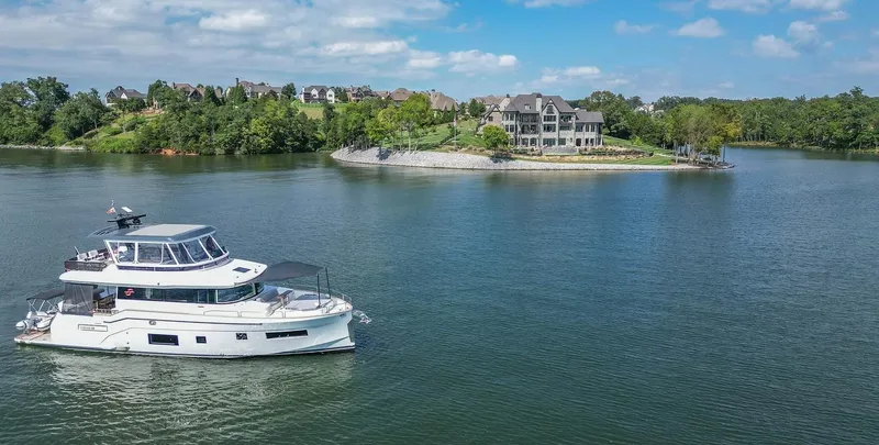 Slide: The Image of Sirena 58 yacht cruising on a serene lake near luxury waterfront homes, 2021 model. - 8