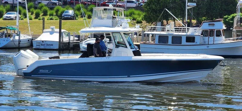 Slide: The Image of 2024 Boston Whaler 330 Outrage boat cruising in a marina with other vessels nearby. - 1