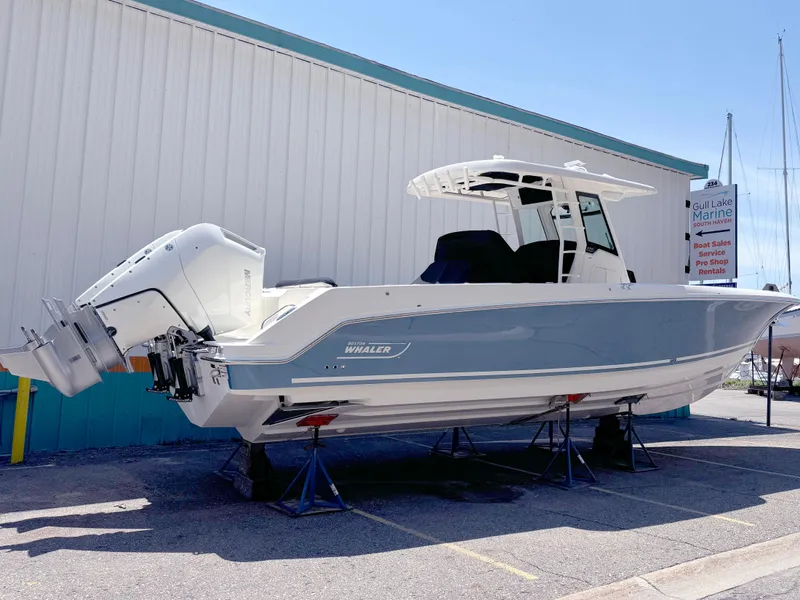 Slide: The Image of 2024 Boston Whaler 330 Outrage boat on stands, side view, near a building. - 3