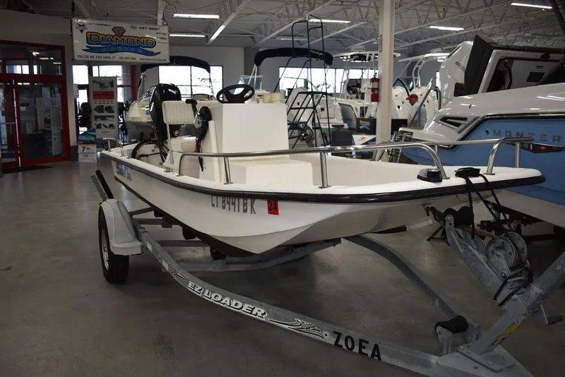 Slide: The Image of 2011 Carolina Skiff J16 boat on trailer in showroom, featuring steering console and outboard motor. - 2
