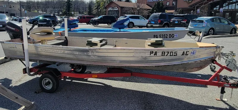 Slide: The Image of 1983 Starcraft SL-14 boat on trailer in parking lot, surrounded by cars. - 0