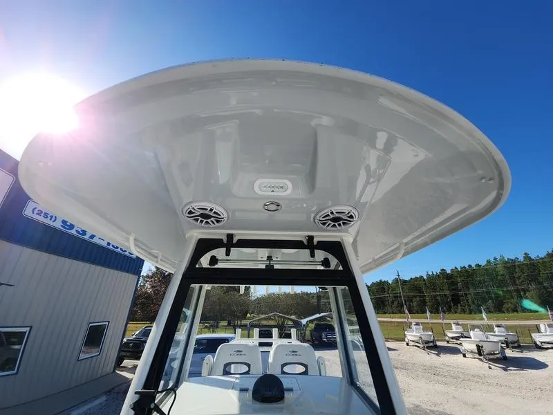 Slide: The Image of 2025 Cobia 265 Center Console boat with T-top and speakers, under clear blue sky. - 12