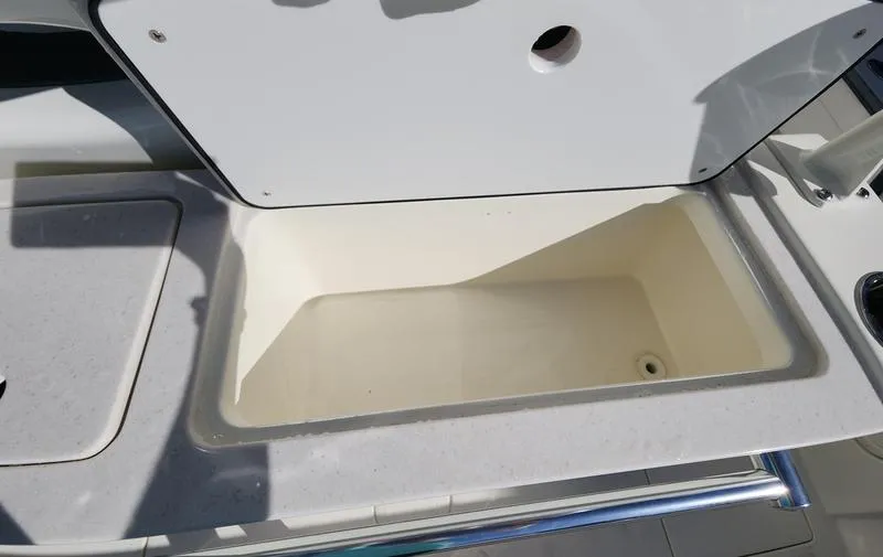 Slide: The Image of 2025 Cobia 265 Center Console boat storage compartment, open lid, white interior. - 32