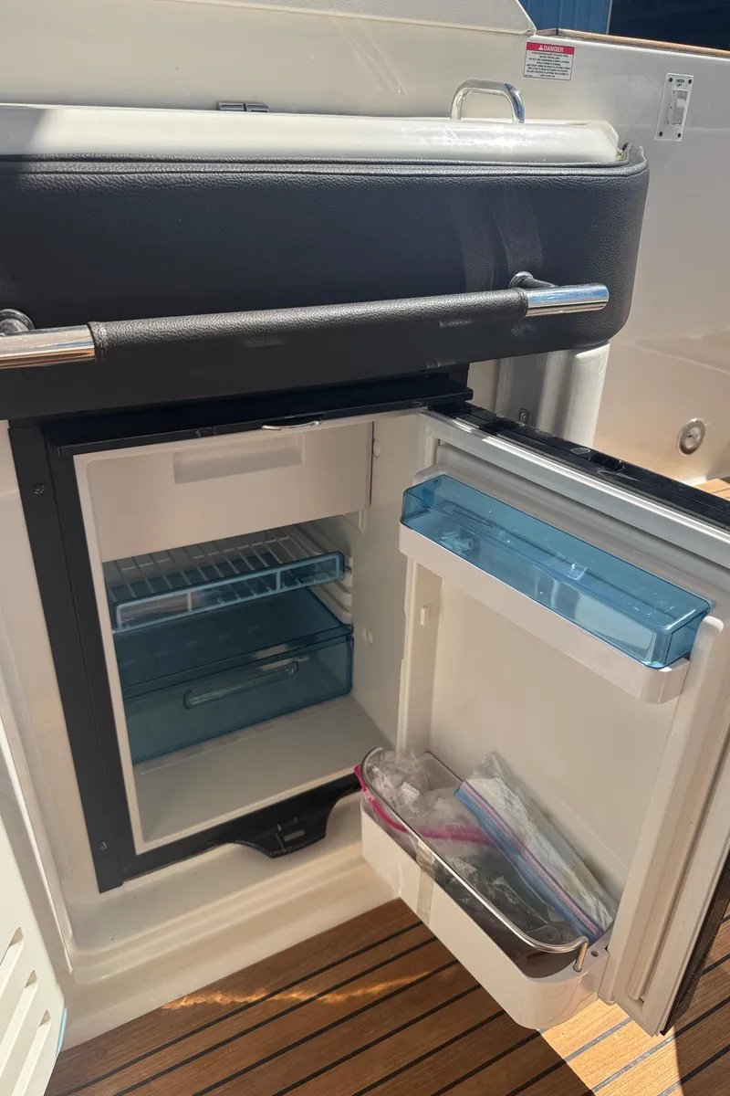 Slide: The Image of 2019 Sea Ray SLX 310 boat refrigerator with open door, showing interior shelves. - 23