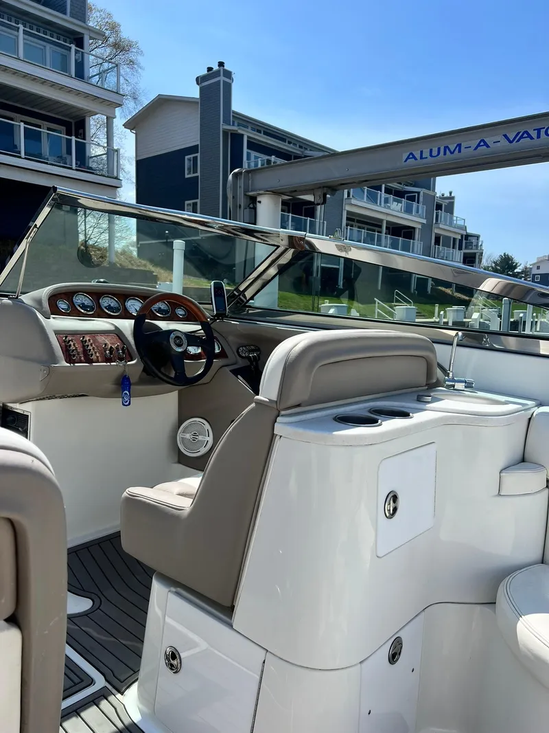 Slide: The Image of 2004 Cobalt 282 boat interior with beige seating and modern dashboard, docked near waterfront buildings. - 2