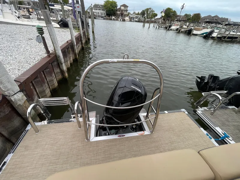 Slide: The Image of 2023 Harris Cruiser 230 boat docked, featuring rear view with motor and water backdrop. - 13