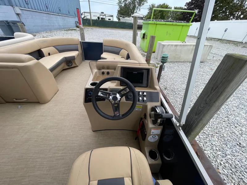 Slide: The Image of 2023 Harris Cruiser 230 boat interior with steering wheel and seating, parked on gravel. - 21