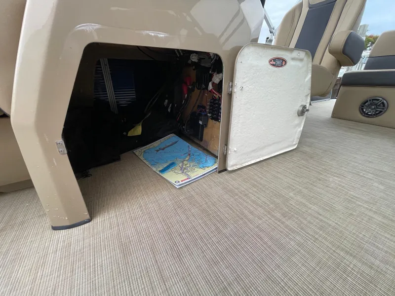 Slide: The Image of 2023 Harris Cruiser 230 storage compartment with open door, revealing interior items and a map. - 28