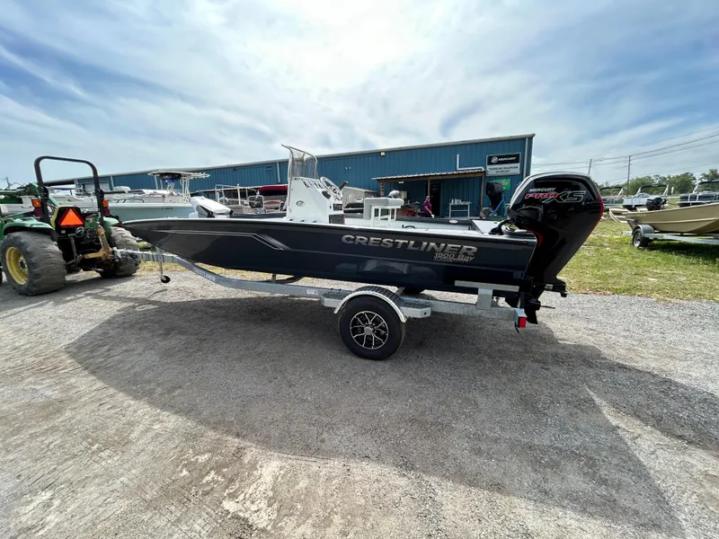 Slide: The Image of 2025 Crestliner 1800 Bay boat on trailer, parked outdoors near a blue building. - 2