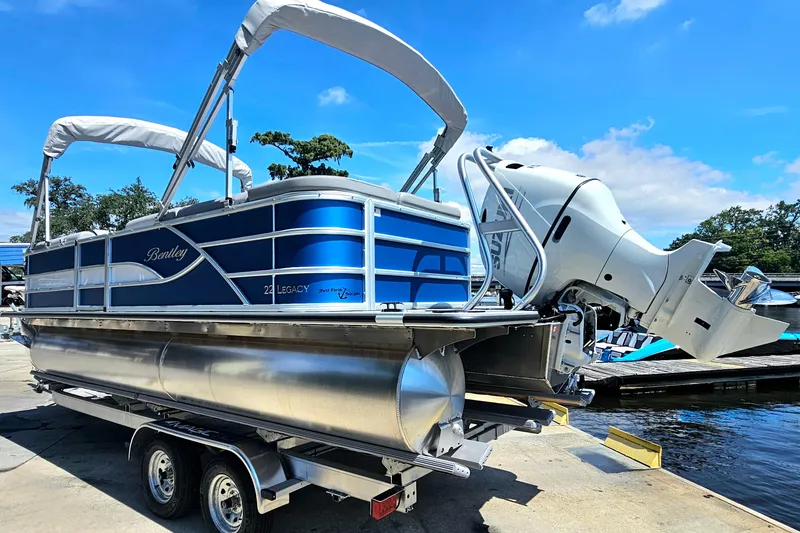 Slide: The Image of 2025 Bentley Pontoons Legacy Cruise 223 on trailer, blue exterior, dockside under clear sky. - 5