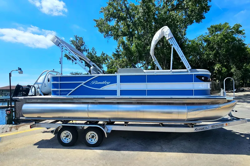 Slide: The Image of 2025 Bentley Pontoons Legacy Cruise 223 on trailer, blue and white design, sunny day. - 8