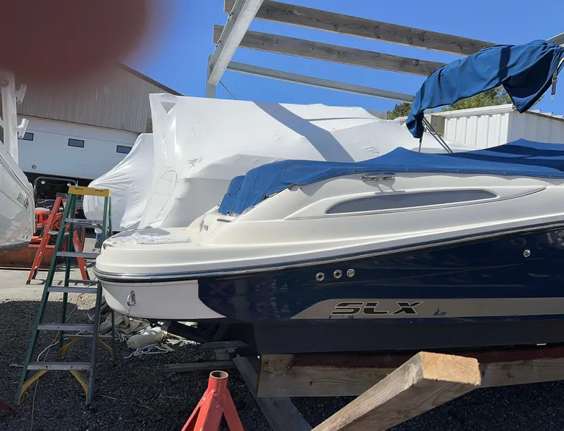 Slide: The Image of 2013 Sea Ray 270 SLX boat in storage, partially covered, with blue and white exterior. - 24