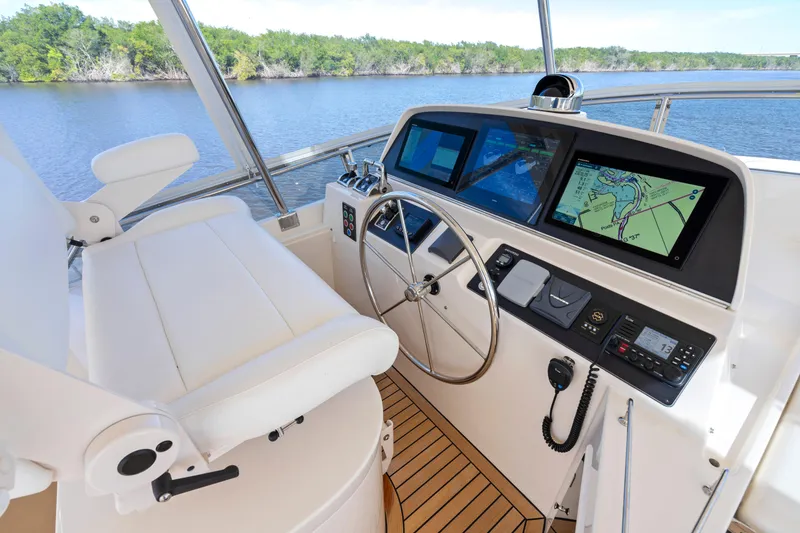 Slide: The Image of 2023 Fleming 65 yacht helm with navigation screens and steering wheel on a serene waterway. - 36