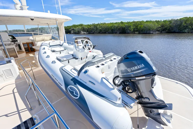 Slide: The Image of 2023 Fleming 65 yacht with Yamaha motorboat on deck, near lush shoreline. - 43