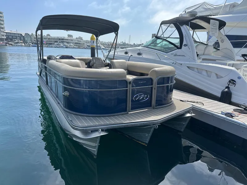 Slide: The Image of 2021 Manitou Oasis SHP pontoon boat docked in a marina, featuring a sleek design and canopy. - 29