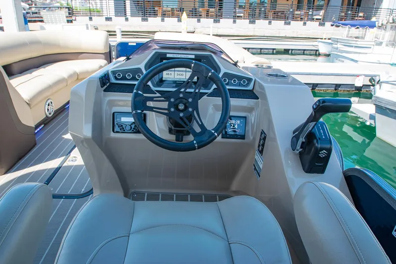 Slide: The Image of 2021 Manitou Oasis SHP boat dashboard with steering wheel and controls at marina. - 49