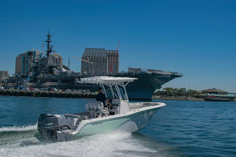 Slide: The Image of 2021 Sea Fox 248 Commander boat cruising near a naval ship and city skyline. - 46