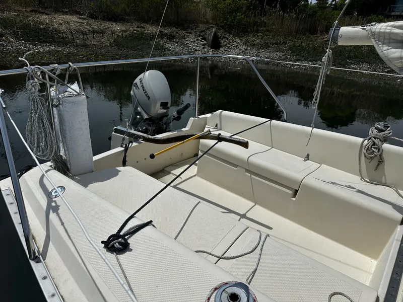 Slide: The Image of 1984 Hunter 25.5 sailboat cockpit with outboard motor, docked by a calm shoreline. - 1