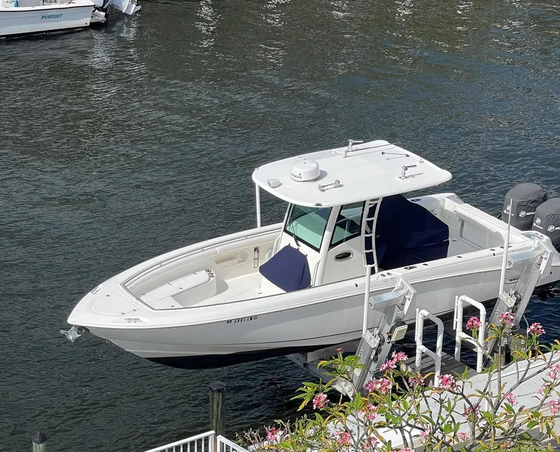 Slide: The Image of 2013 Boston Whaler 320 Outrage boat docked on calm water, surrounded by flowers. - 4