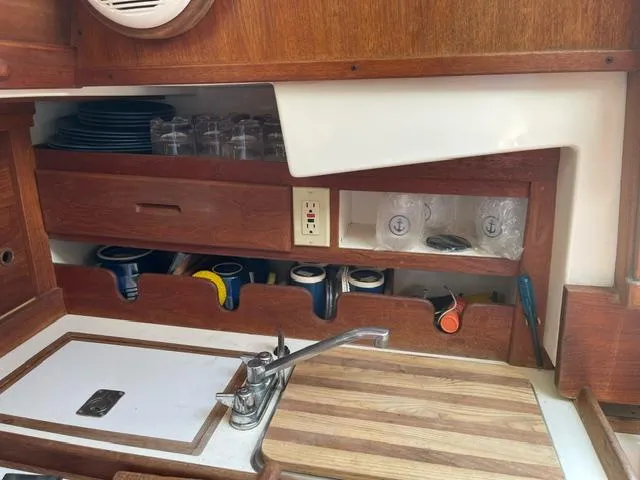 Slide: The Image of 1984 Tartan T-33 yacht kitchen with wooden cabinetry, sink, and organized storage for dishes and mugs. - 21
