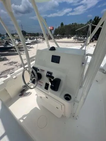 Slide: The Image of 2024 Cobia 220 CC boat console with steering wheel and controls under a clear blue sky. - 10