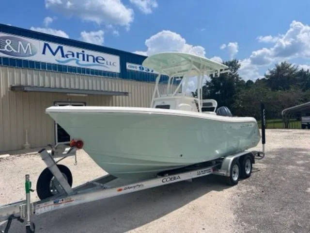 Slide: The Image of 2024 Cobia 220 CC boat on trailer outside marine dealership under blue sky. - 3