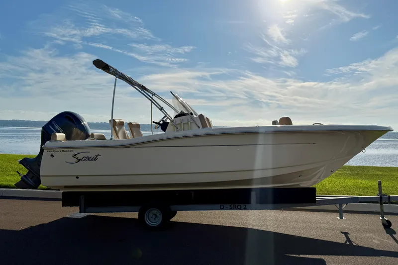 Slide: The Image of 2025 Scout 195 Sport Dorado boat on trailer by waterfront under clear sky. - 2