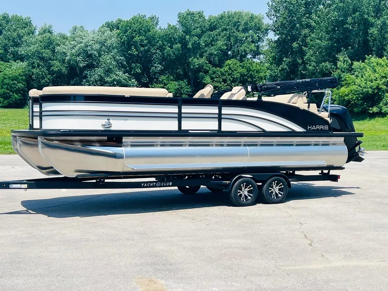 Slide: The Image of 2025 Harris Sunliner 230 pontoon boat on trailer, parked outdoors with trees in background. - 2