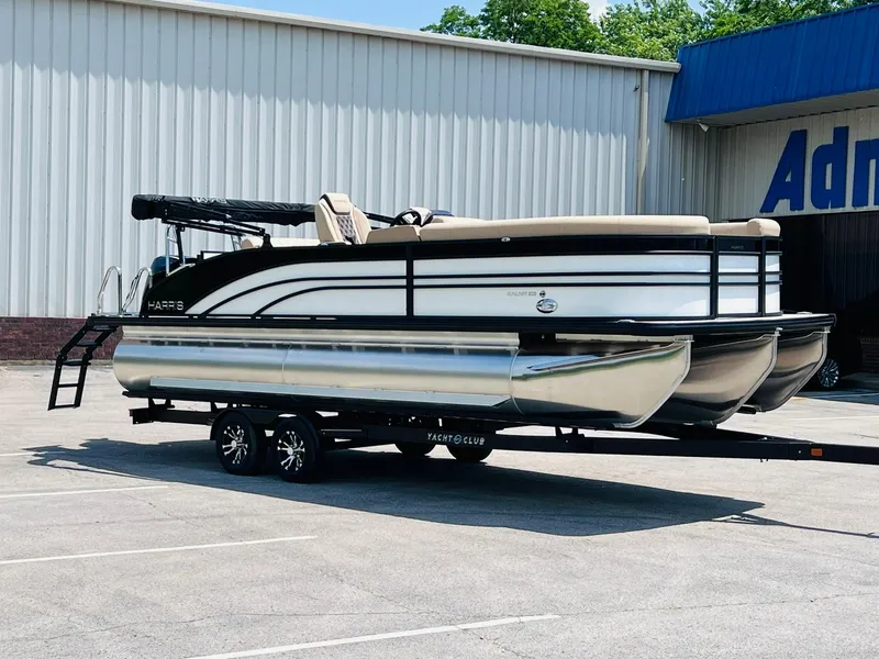 Slide: The Image of 2025 Harris Sunliner 230 pontoon boat on trailer, parked outside a building. - 3
