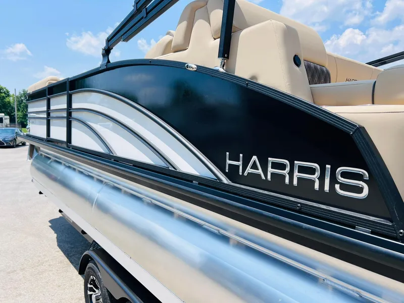 Slide: The Image of 2025 Harris Sunliner 230 pontoon boat with sleek black and silver design under a clear sky. - 5