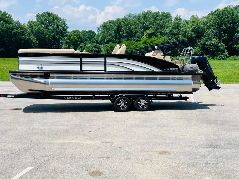 Slide: The Image of 2025 Harris Sunliner 230 pontoon boat on trailer, parked outdoors with trees in background. - 6