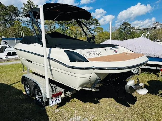 Slide: The Image of 2021 Stingray 225 SE boat on trailer, parked outdoors under blue sky. - 2