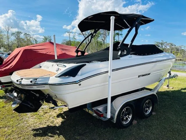Slide: The Image of 2021 Stingray 225 SE boat on trailer, black canopy, parked outdoors under blue sky. - 7